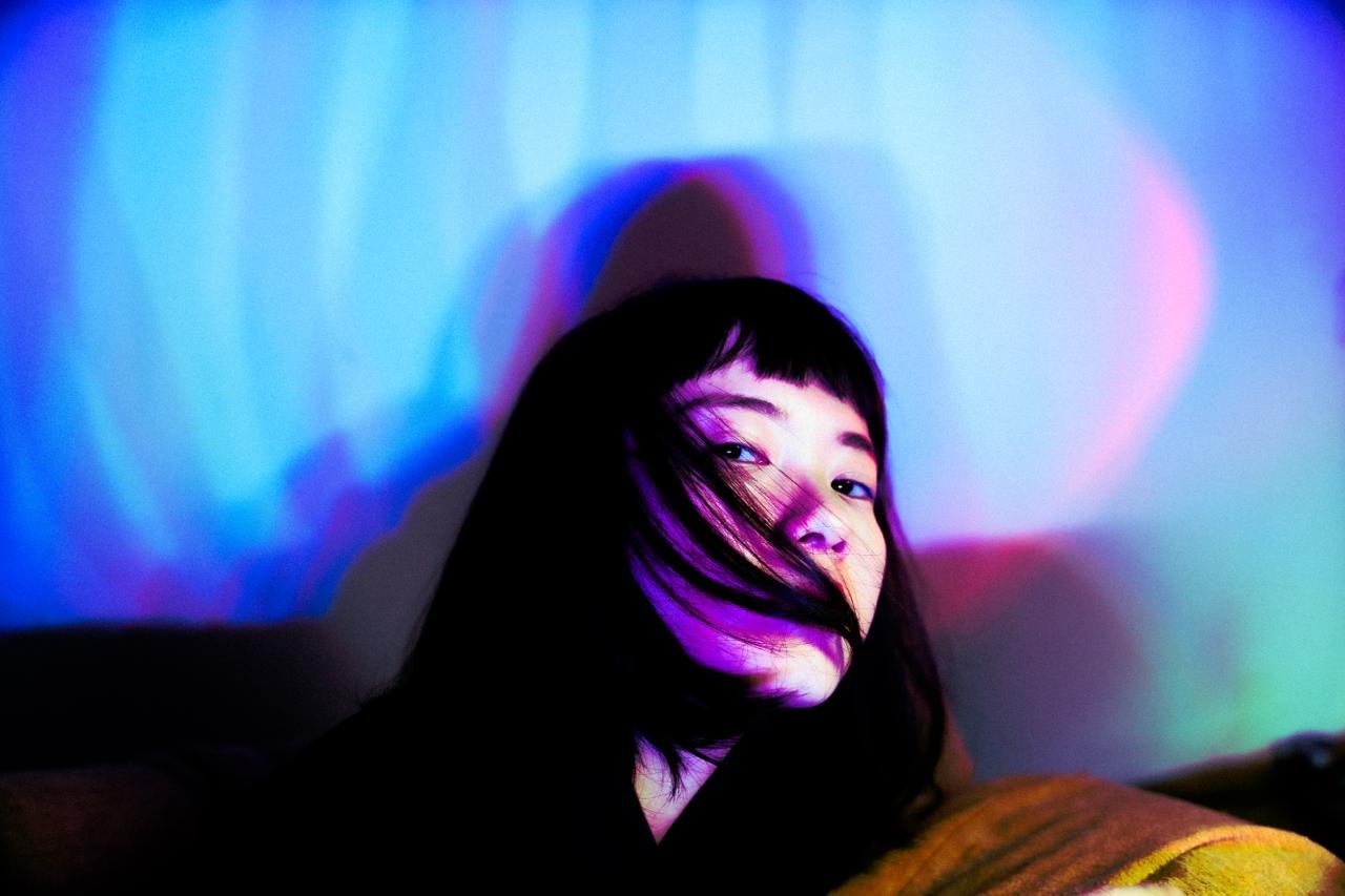 A woman's face in blue and pink light, hair across her face