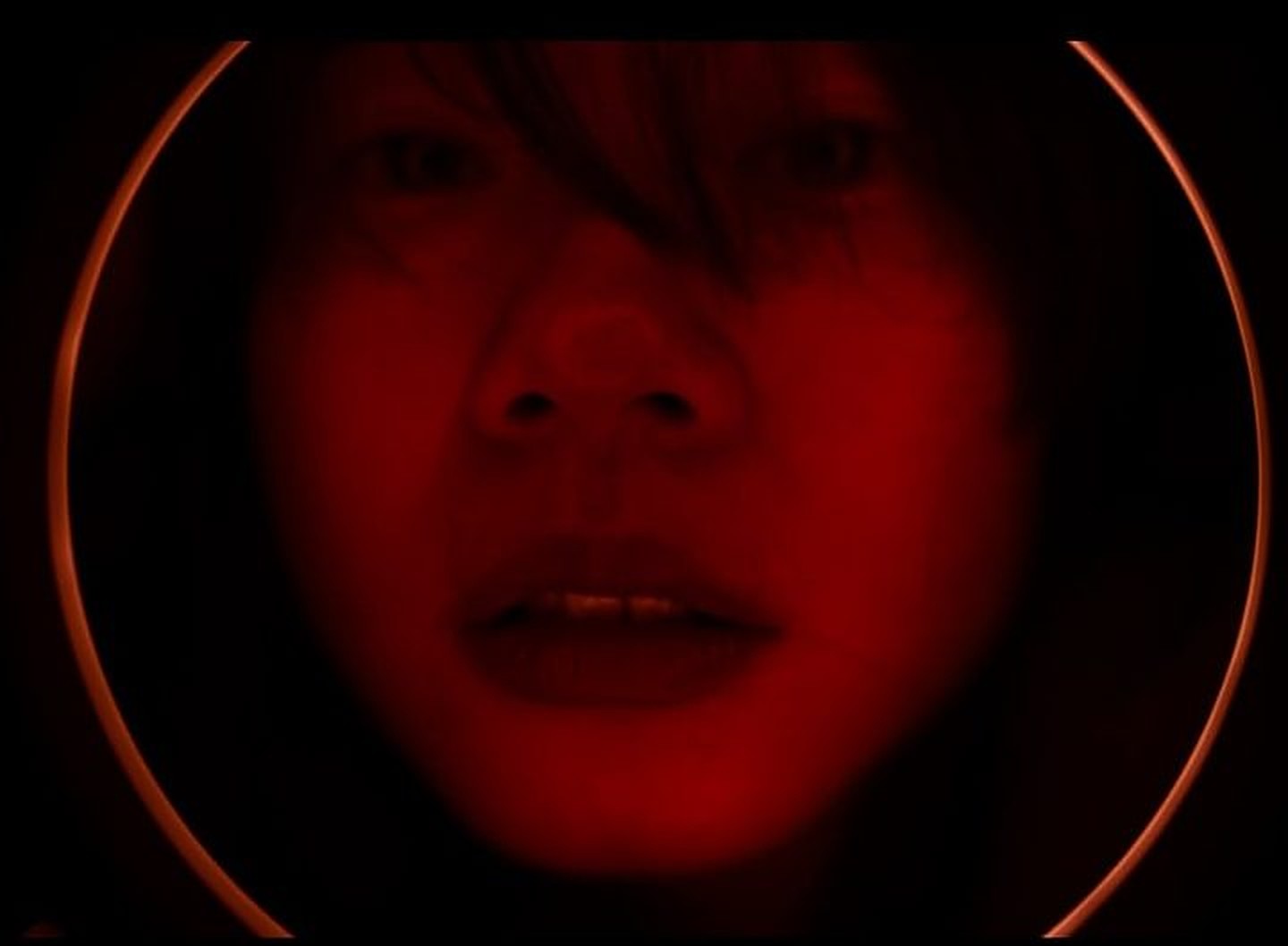 A face lit red inside a glowing ring light
