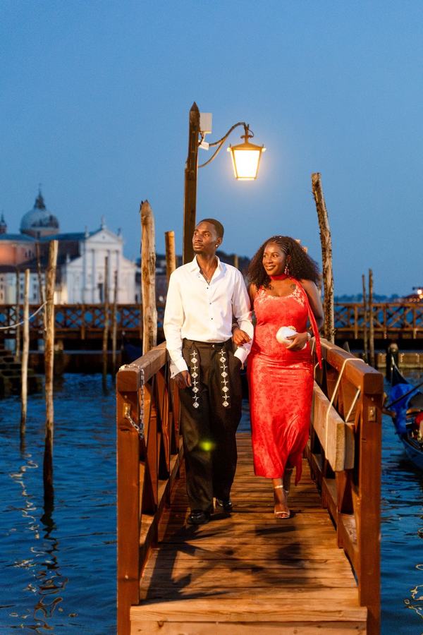 A couple walking arm in arm on a pier at blue hour below a lit lantern