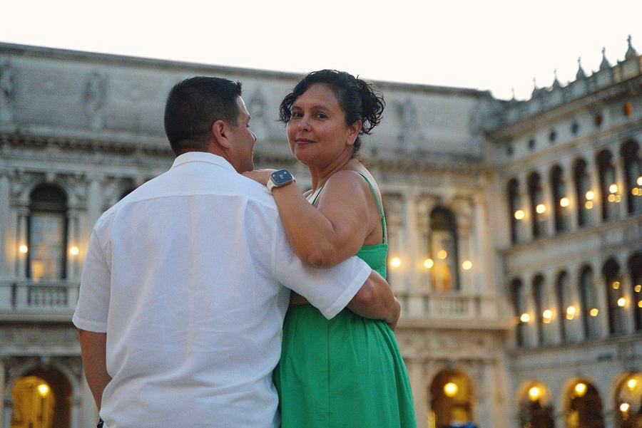 A man and a woman in a green dress embracing in St Mark's Square at dusk