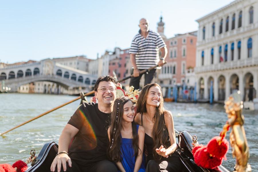 A family laughing on a gondola on the Grand Canal, the Rialto Bridge behind them