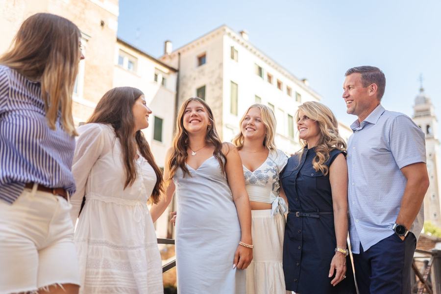 A family laughing together in the sun in Venice, a bell tower behind them