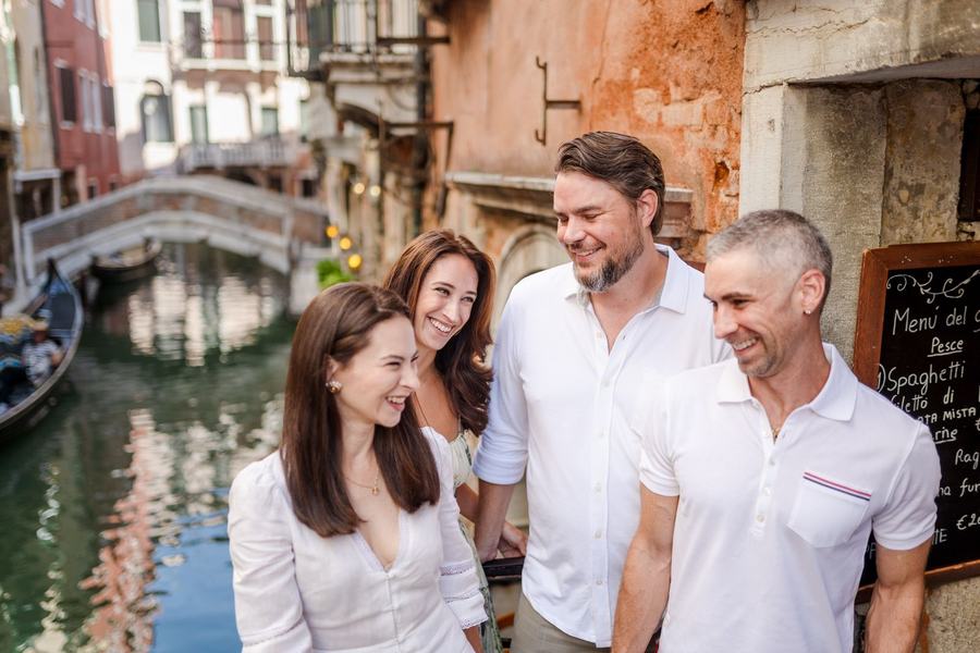 Four friends laughing together beside a canal in Venice