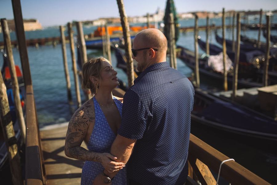 A couple looking at each other on a wooden pier beside moored gondolas in Venice