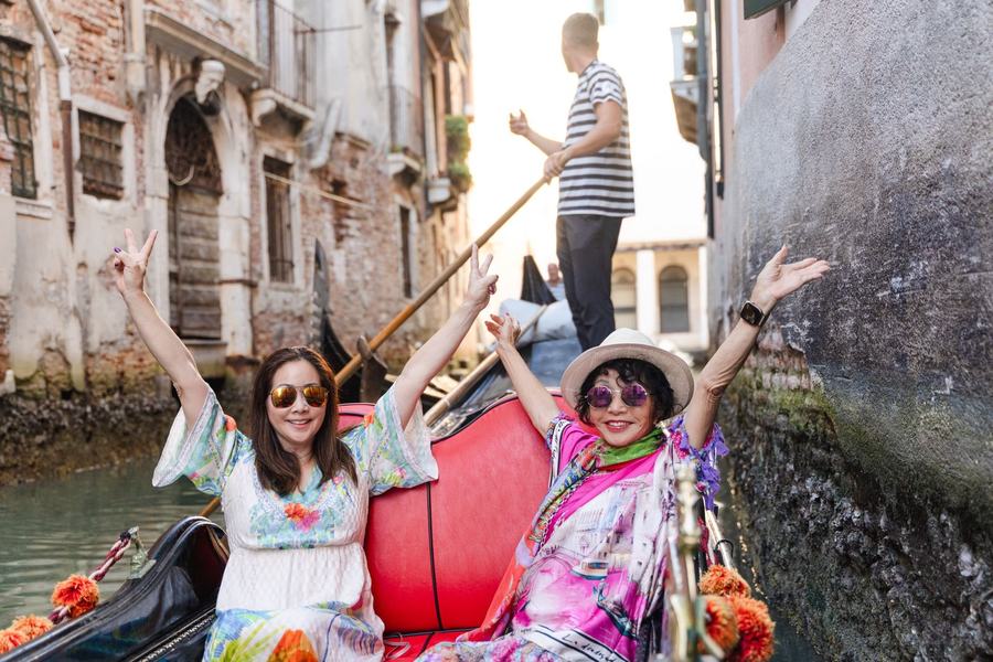 A mother and daughter cheering with their arms up on a gondola in a narrow canal