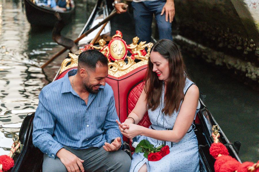 A woman looking at her new ring on a gondola, red roses on her lap