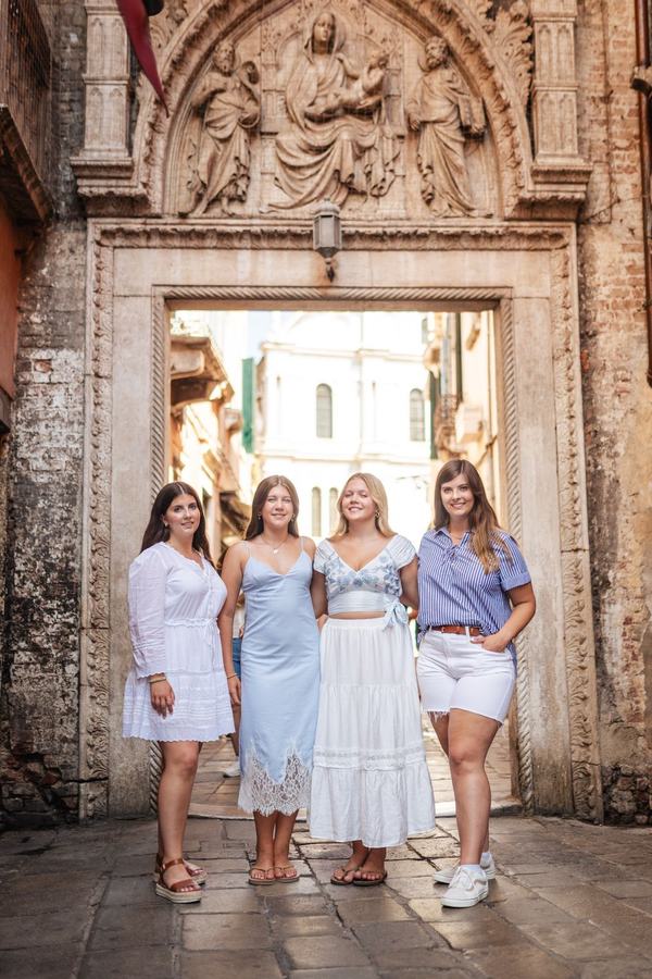 Four sisters standing under a carved stone archway in Venice