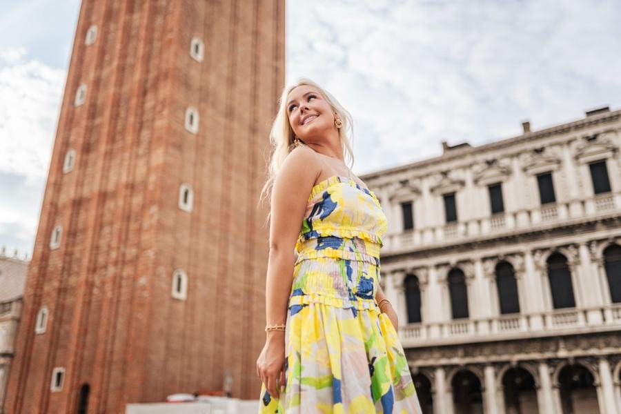 A woman in a yellow dress looking up below the bell tower of St Mark's