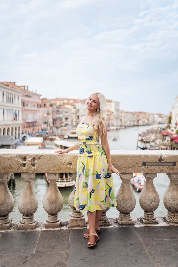 A woman in a yellow dress on the Rialto Bridge with the Grand Canal behind her