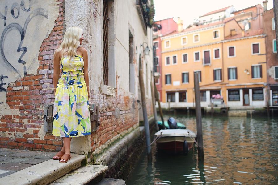 A woman in a yellow floral dress at the edge of a Venetian canal
